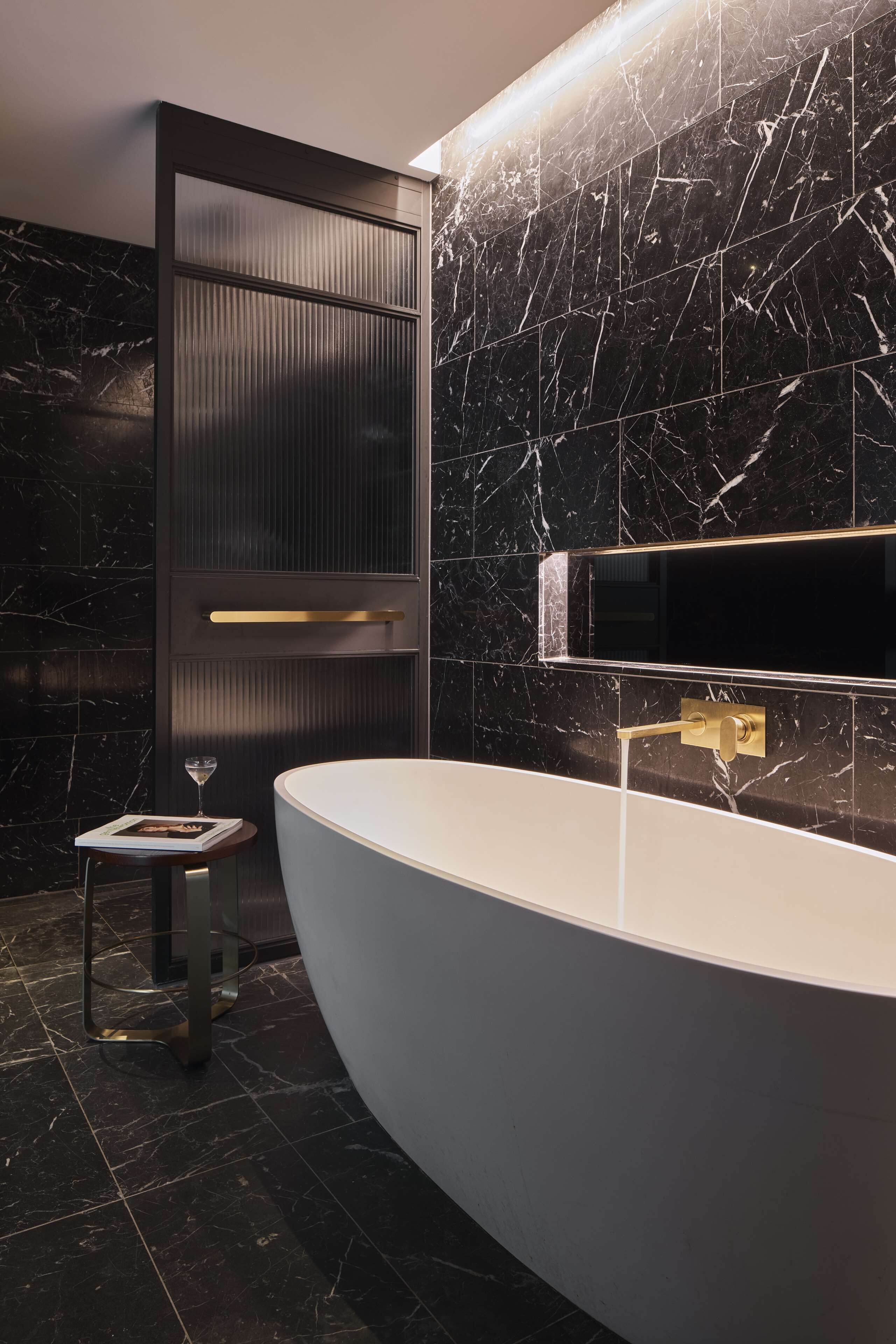 A modern bathroom with a large white bathtub, dark marble walls, and a minimalist design.