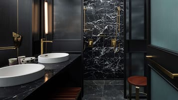 A modern bathroom with two sinks, a shower, and a stool.