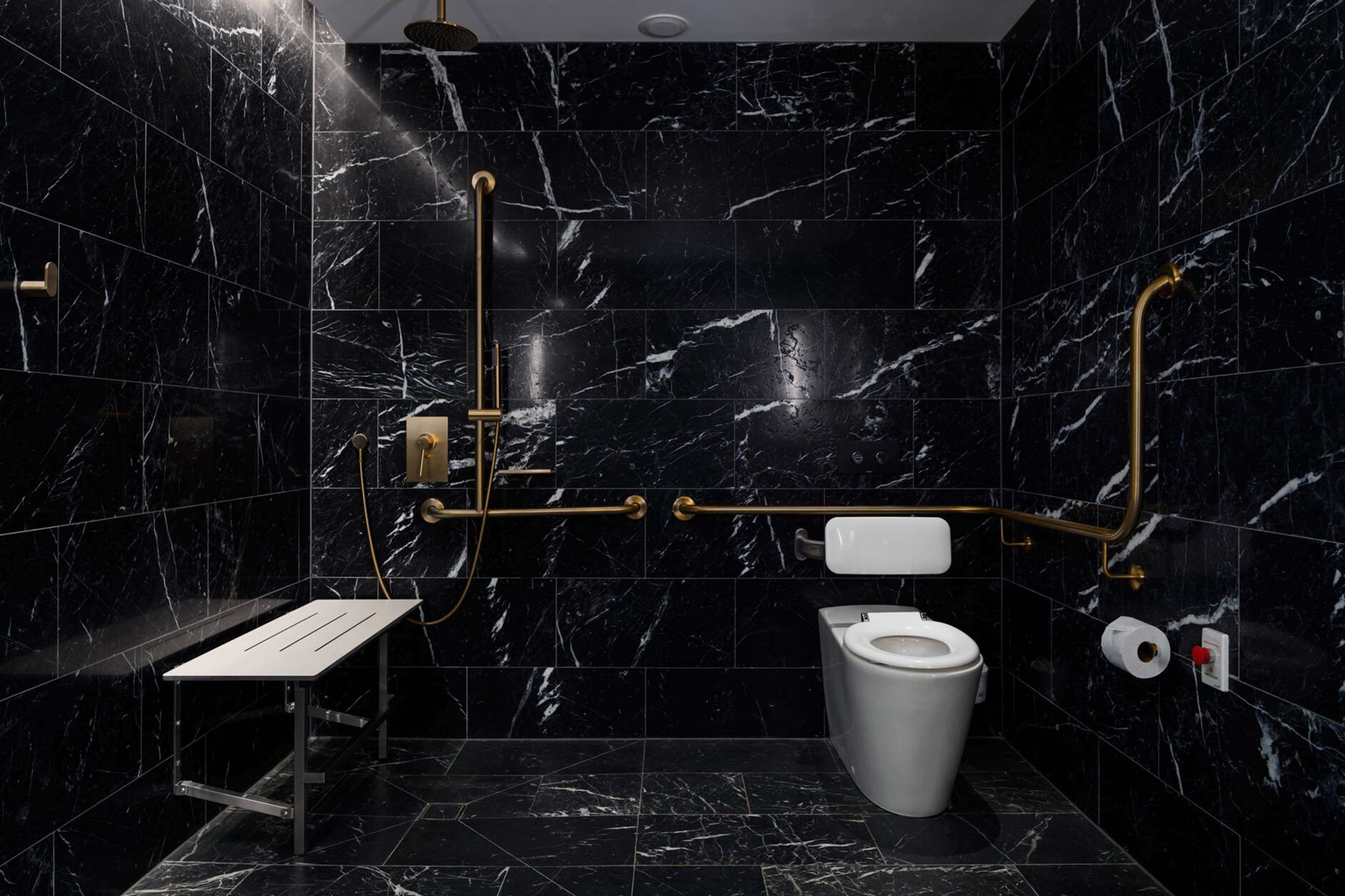 A modern bathroom with black marble tiles, a white toilet, a sink with a gold faucet, and a shower area.
