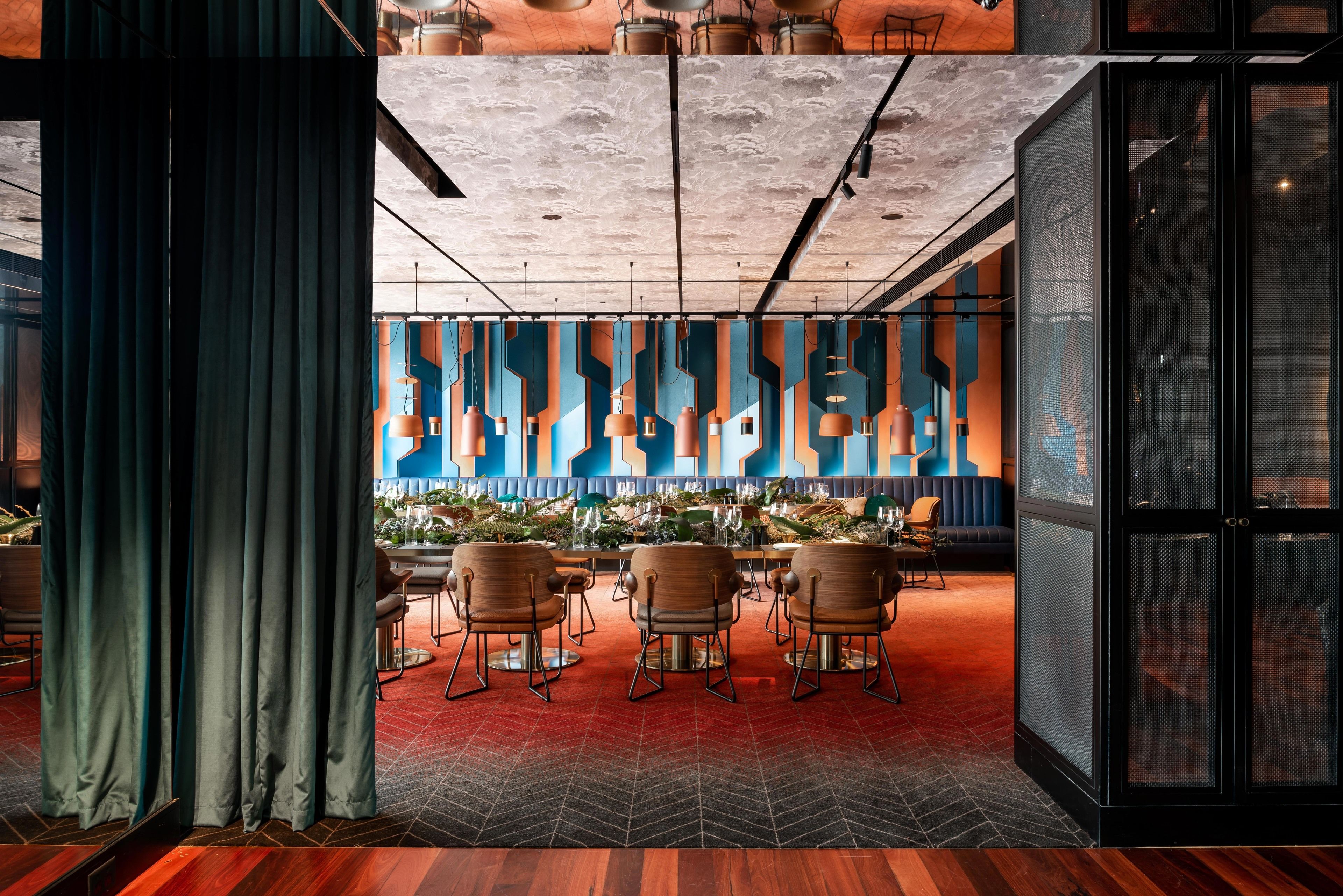 A modern conference room with a red herring floor, wooden chairs, and a blue and orange abstract wall design.
