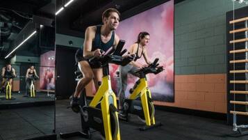 Un gimnasio con bicicletas estáticas, un espejo y una pared de ladrillo.