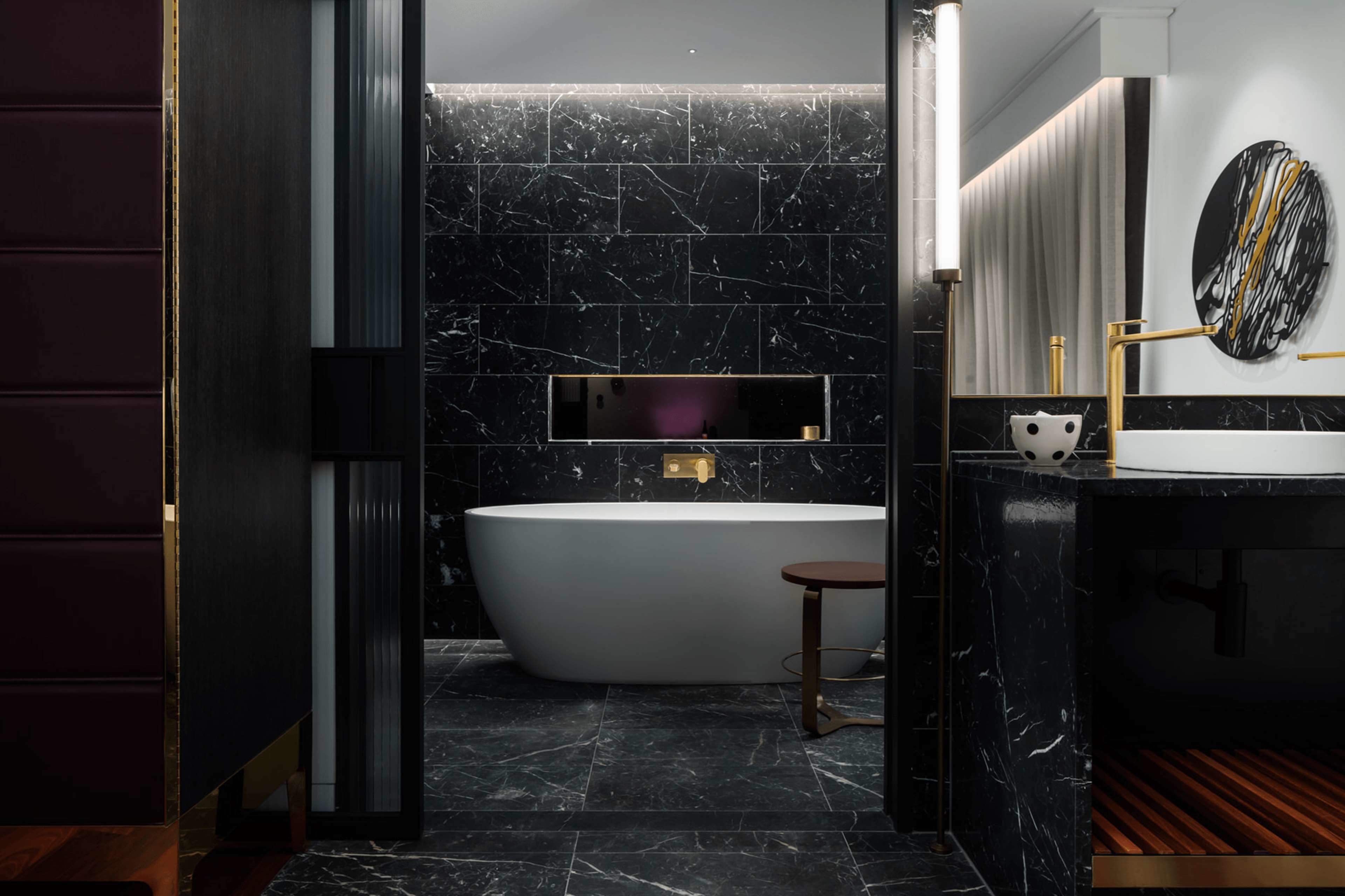 A modern bathroom with a freestanding bathtub, a vanity with a mirror, and a marble-tiled wall.