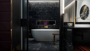 A modern bathroom with a freestanding bathtub, a vanity with a mirror, and a marble-tiled wall.