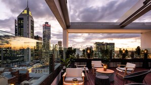 A rooftop terrace with seating and a city view at dusk. - QT Perth (Perth)