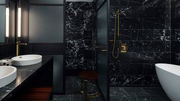 Un baño moderno con baldosas de mármol negro, un lavamanos blanco, una bañera grande y un cabezal de ducha dorado.