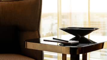 A modern room with a dark brown armchair, a small table with a black object, and a view of a cityscape through large windows.