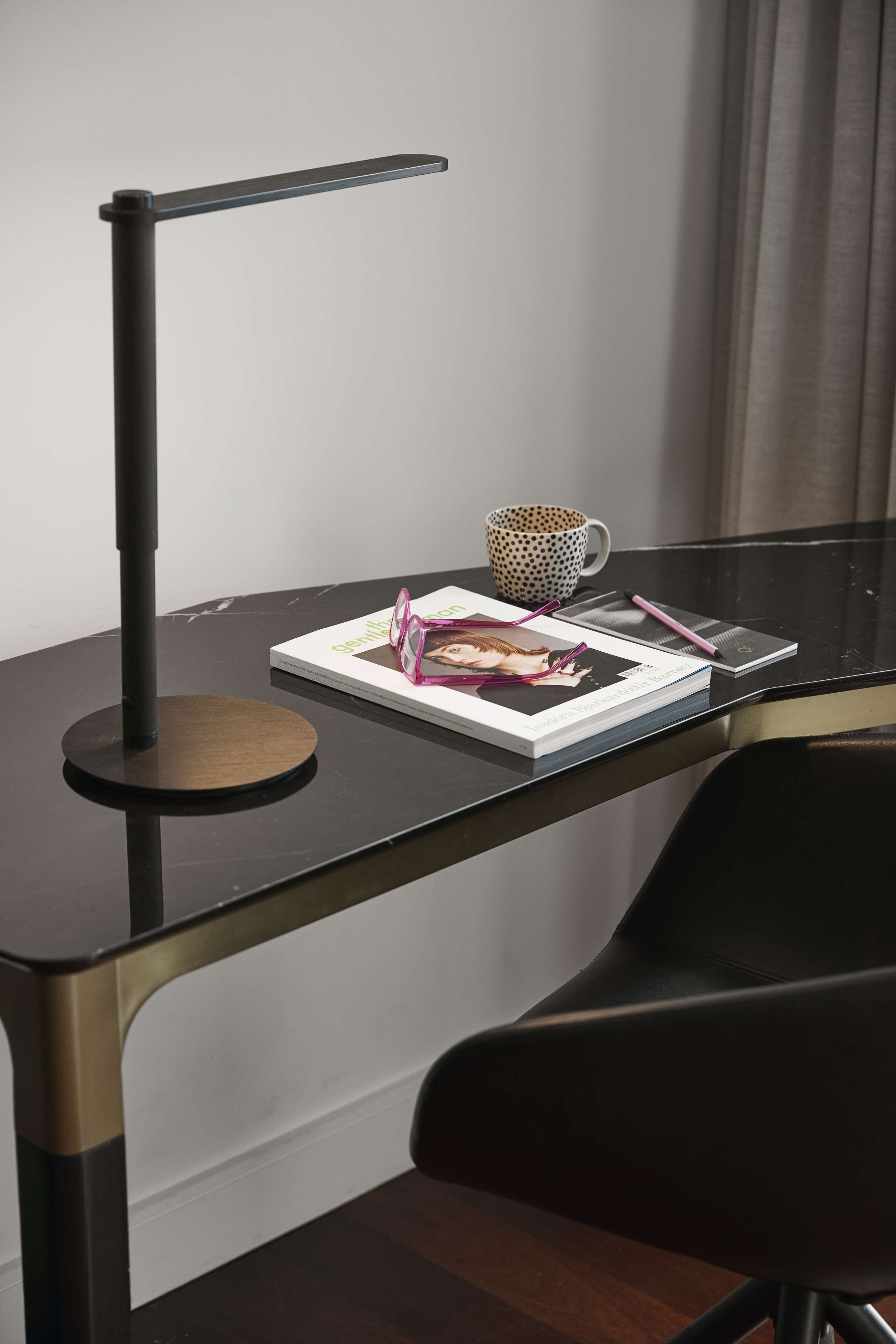 A modern desk with a black lamp, a polka-dotted mug, a book, and a smartphone.