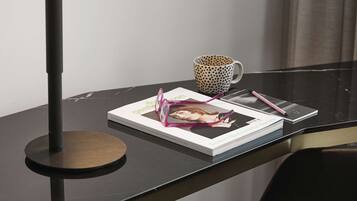 A modern desk with a black lamp, a polka-dotted mug, a book, and a smartphone.