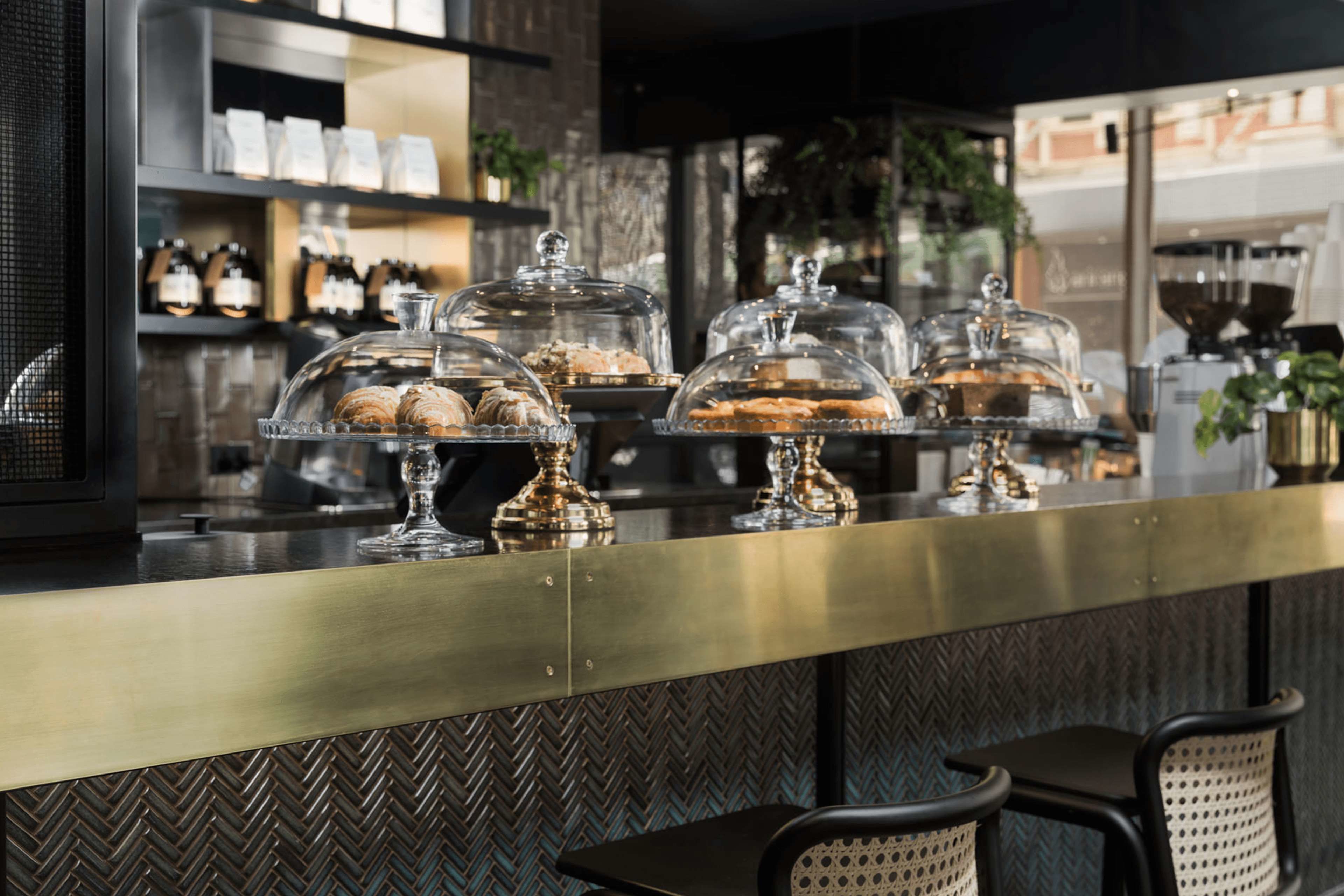 A bakery counter with pastries under glass domes, a coffee machine, and seating area.