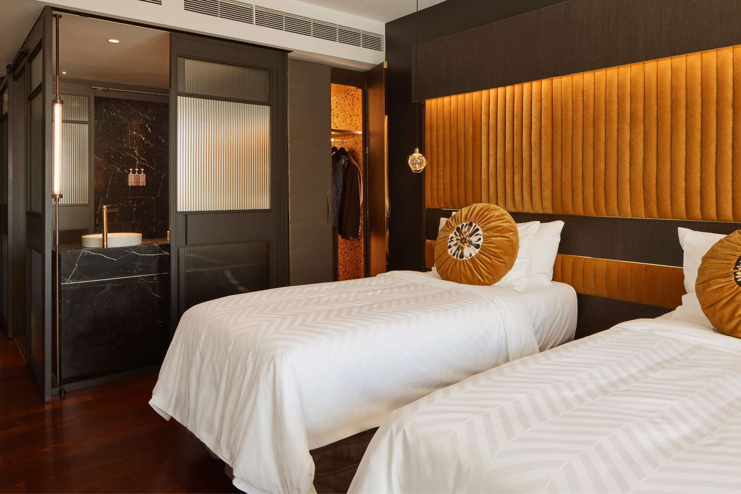 A hotel room with two beds, a large mirror, a vanity with a sink, and a wardrobe.