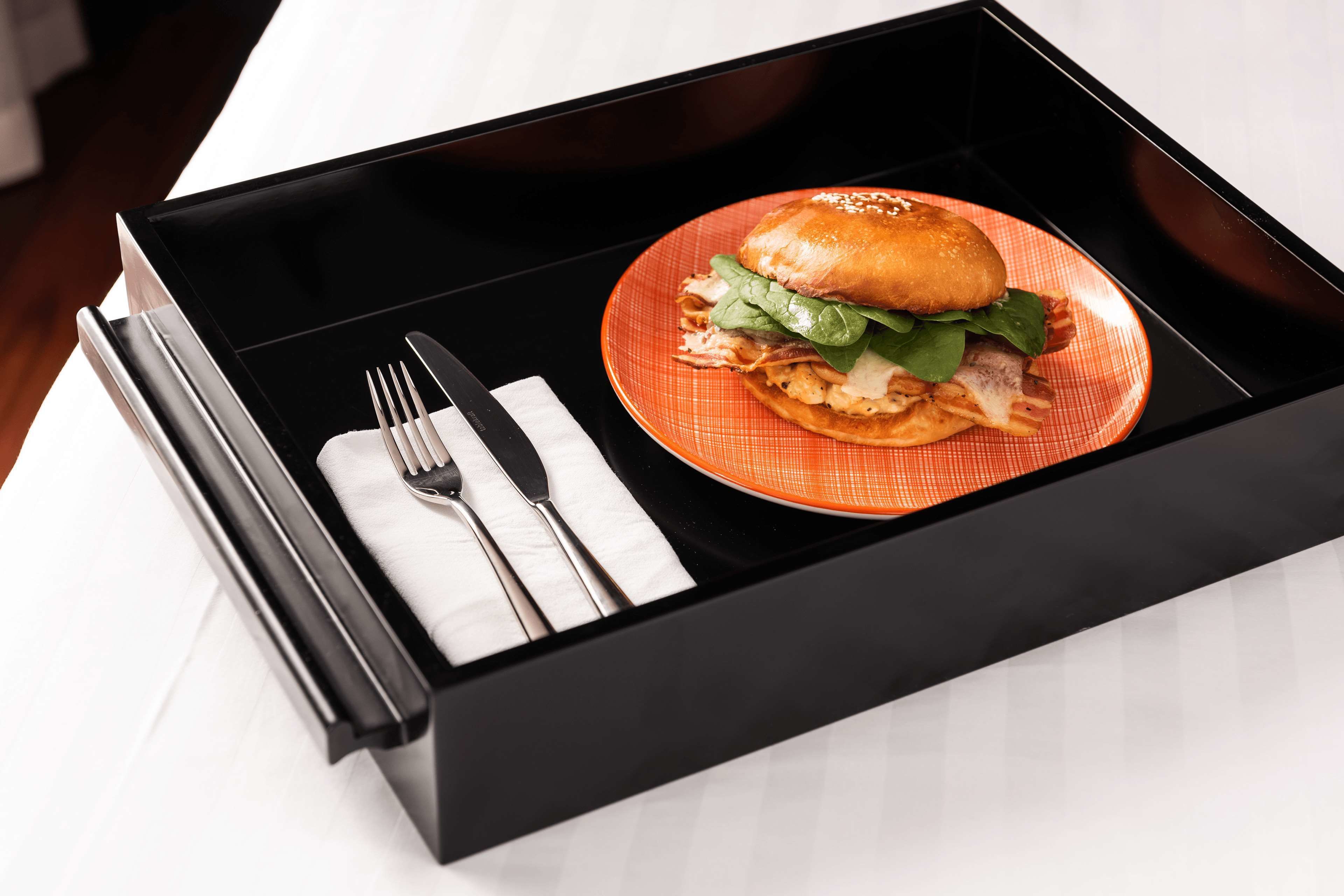 Una bandeja negra con una hamburguesa sobre un plato naranja, un tenedor y un cuchillo sobre una servilleta blanca.
