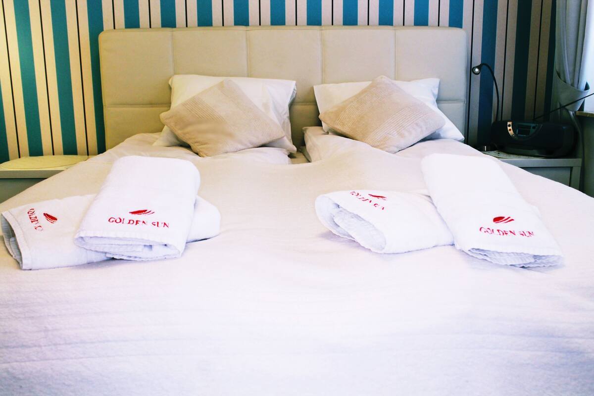 A hotel room with a large bed, two pillows, and two folded towels with a logo.