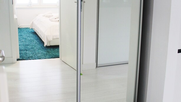 A modern bedroom with a glass door leading to a bathroom, a blue carpet, and a black doormat. - Golden Sun Apartments  - Grzybowo (Kolobrzeg)