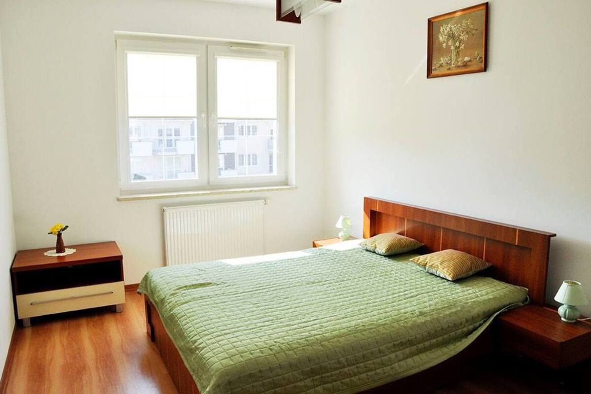 A bedroom with a bed, a nightstand, a dresser, a window, and a framed picture on the wall.