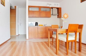 Une cuisine de taille réduite, avec des meubles de rangement en bois, une table à manger avec des chaises et un vase avec une fleur.