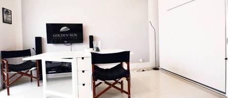 A room with a white desk, two black chairs, a flat-screen TV on the wall, and a closed door.