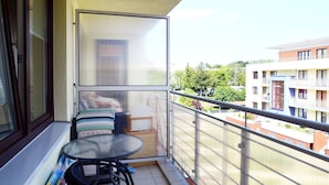Un balcón con una mesa y sillas, una ventana y vistas a edificios y zonas verdes.