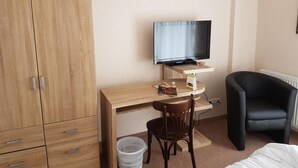 Un dormitorio con un armario de madera, un escritorio con silla, un televisor y un sillón negro.