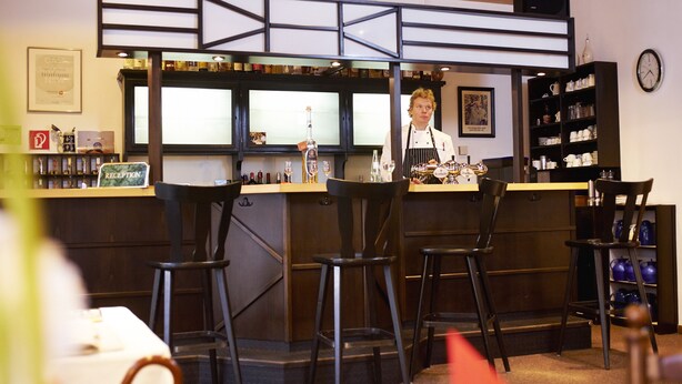 Zona de bar con taburetes, una recepción y estantes con botellas y vasos.