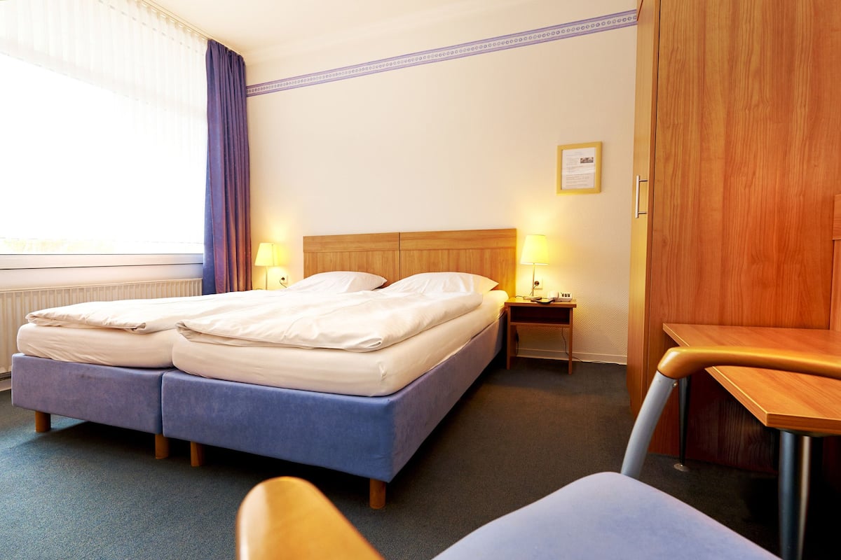 A hotel room with a double bed, two bedside tables with lamps, a wooden wardrobe, and a chair.