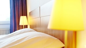 Una habitación de hotel con una cama bien hecha, una lámpara de noche y una ventana con cortinas.