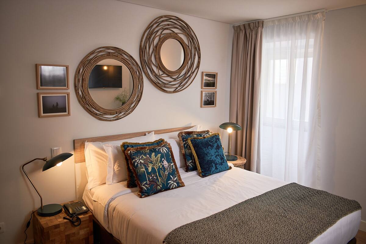 A neatly arranged bedroom with a bed, bedside lamps, and decorative mirrors on the wall.