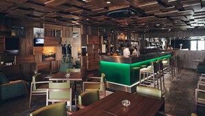 A bar area with wooden paneling, a green-lit bar counter, and seating with tables and chairs. - Hotel Cruzeiro (Angra do Heroismo)