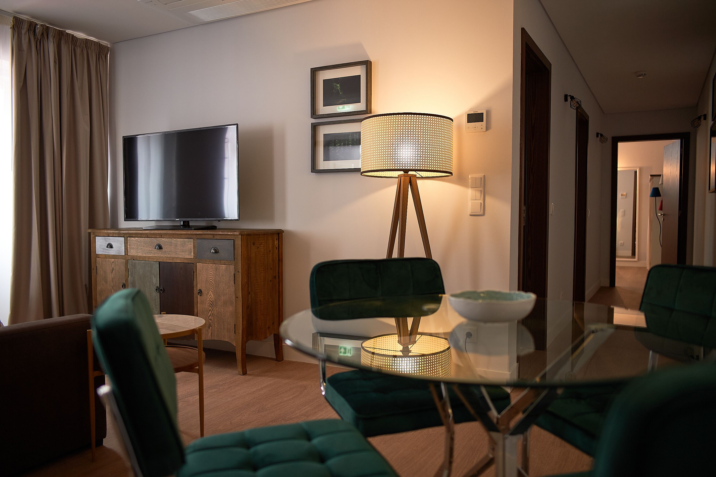 A modern hotel room with a flat-screen TV, a glass table, and green upholstered chairs.