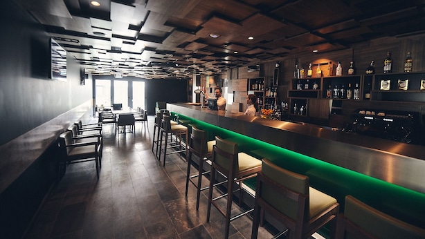 A bar area with a long counter, stools, and a variety of bottles on shelves. - Hotel Cruzeiro (Angra do Heroismo)