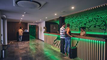 A reception area with a wooden reception desk, a green illuminated wall, and a tiled floor.