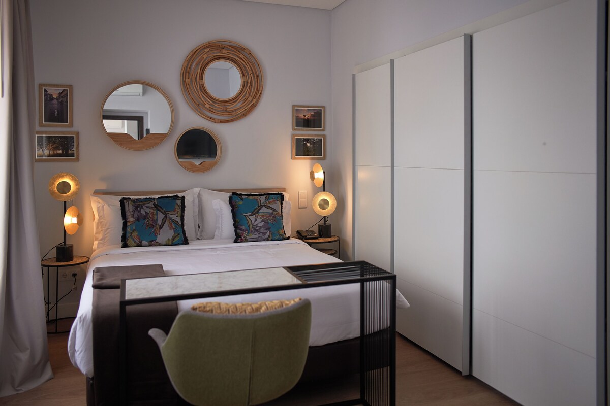 Quarto moderno com cama, abajures, espelho redondo e quadros na parede.