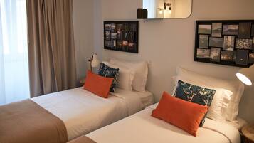Habitación de hotel con dos camas, ropa de cama color beige y almohadas naranjas. Hay marcos de cuadros en la pared y un espejo sobre las camas.