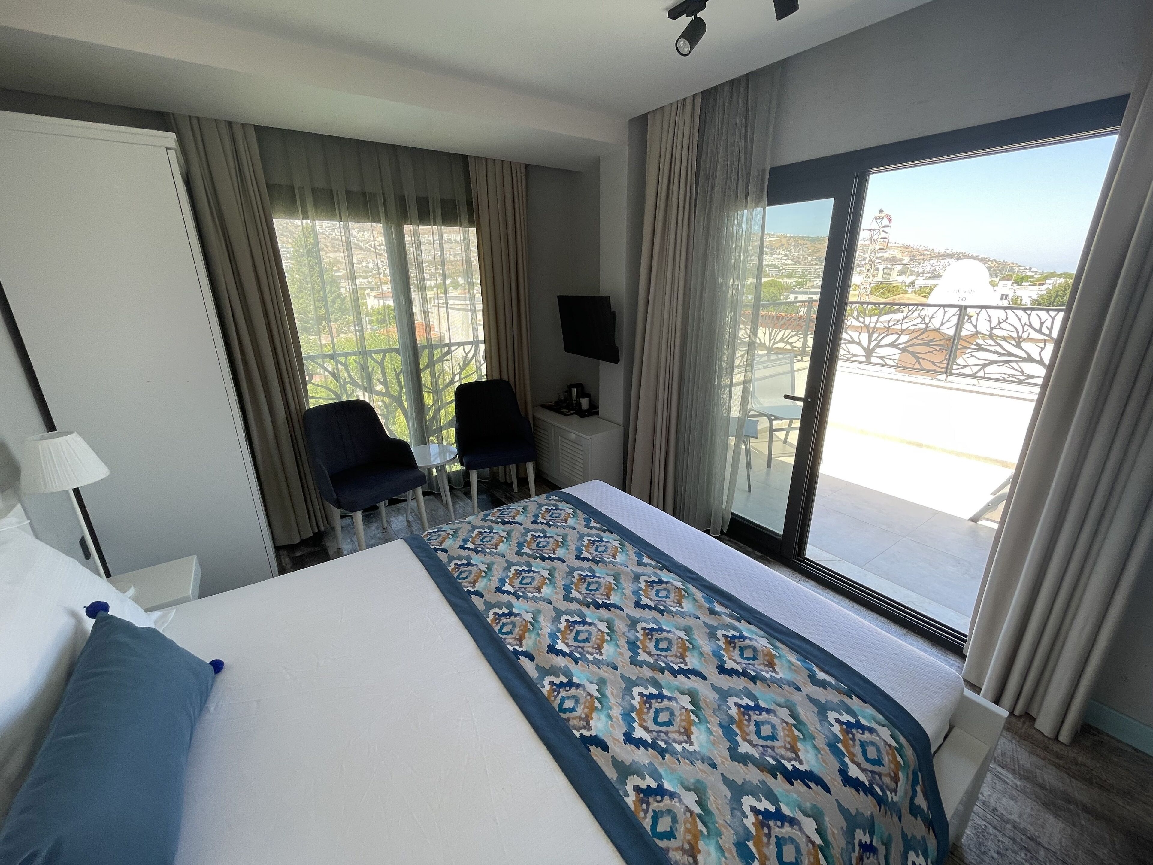 A hotel room with a large bed, a desk with two chairs, a TV, and a balcony with a view of the city.