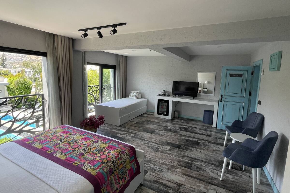 Une chambre d’hôtel avec un lit, un bureau avec une télévision, un balcon donnant sur une piscine et une porte bleue.