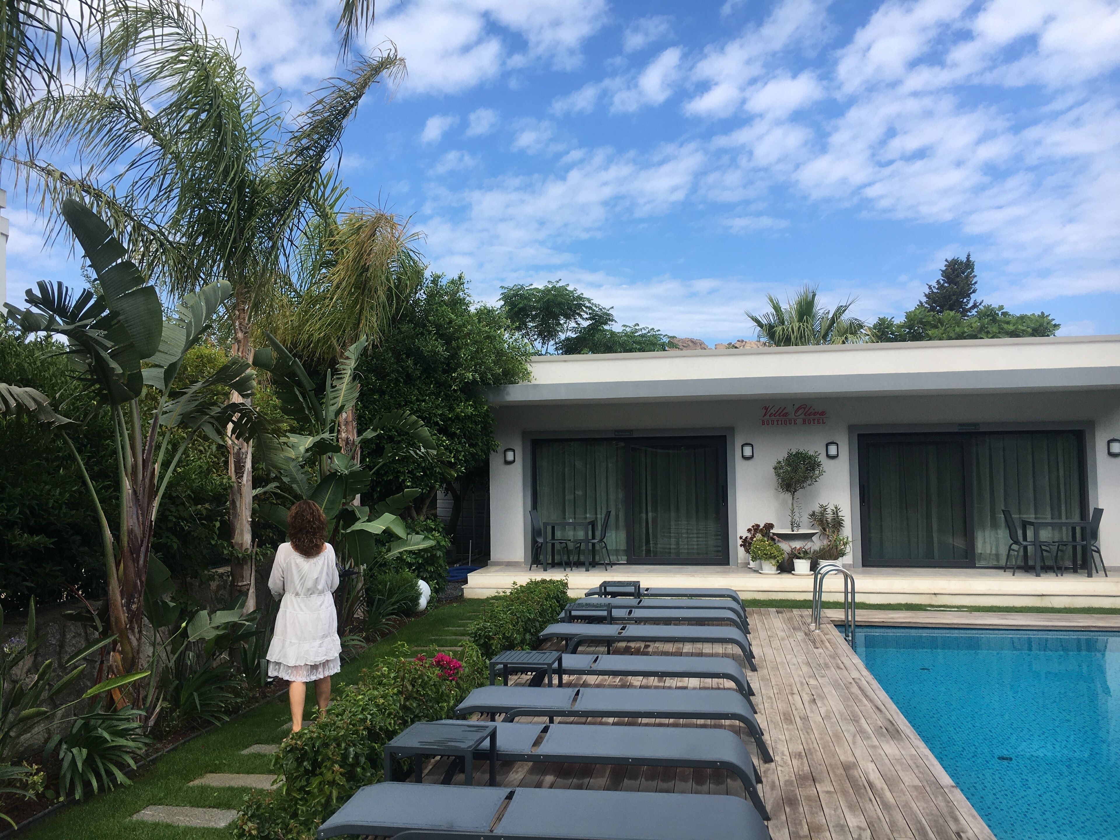 Un hotel con piscina, mobiliario exterior y abundante vegetación.