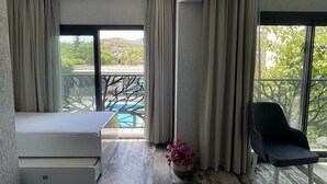 Camera d'albergo moderna con un letto, una sedia, un tavolino e vista su una piscina e del verde all'esterno.