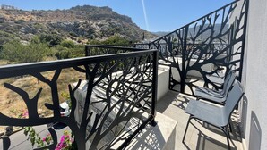 Un balcone con ringhiera in metallo, un tavolo e sedie. Si vede una montagna sullo sfondo.