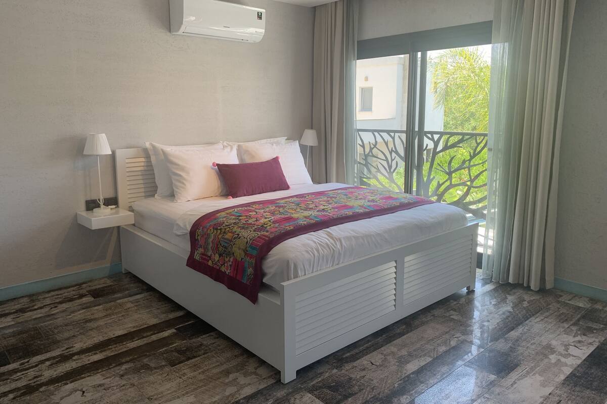 Une chambre à coucher avec un lit, des lampes de chevet, une fenêtre donnant sur un beau paysage et un appareil de climatisation.