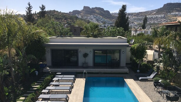 Una piscina con lettini, una zona relax coperta e vista su una cittadina collinare.