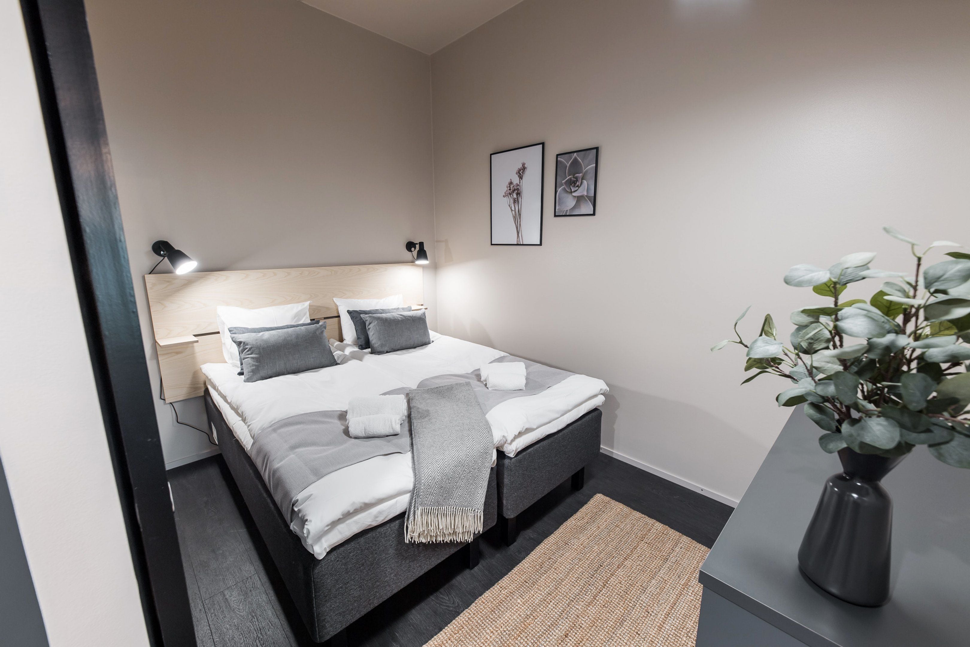 Un dormitorio ordenado con cama, lámparas de noche, mesitas de noche y una planta en maceta.
