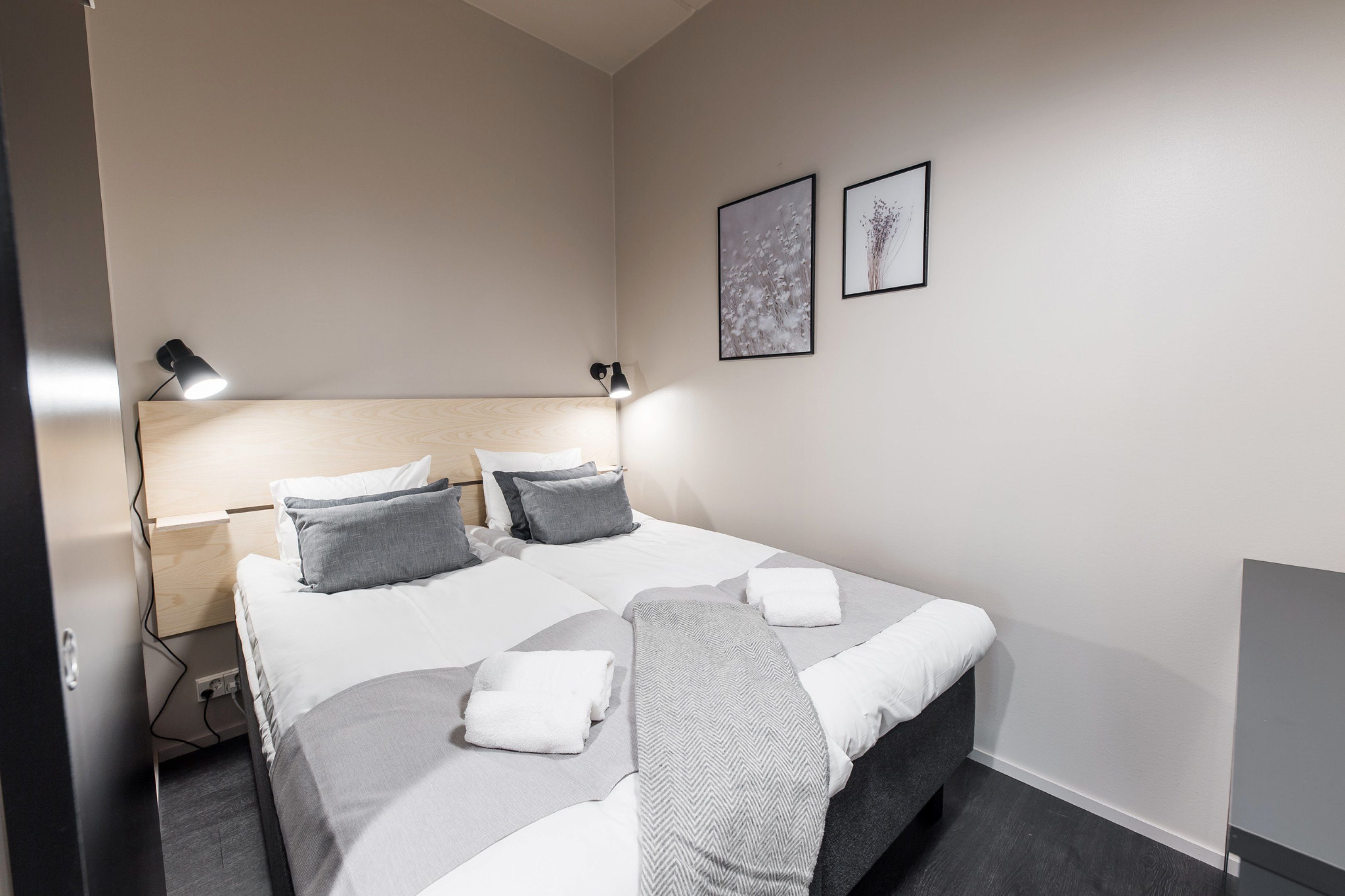 Un dormitorio ordenado con cama, mesitas de noche y lámparas de pared.