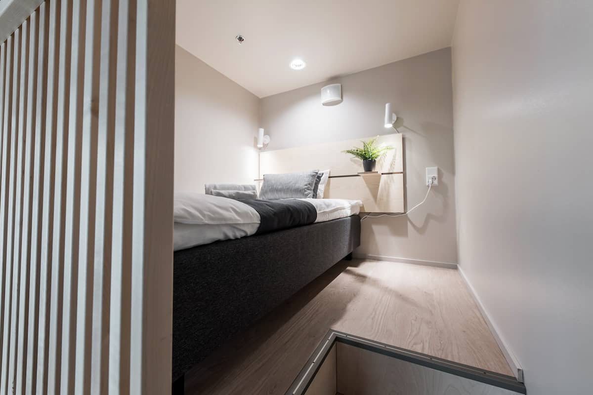 A compact bedroom with a bed, bedside table, and a wall-mounted shelf with a plant.