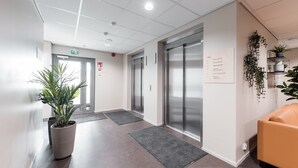 A modern hotel lobby with a reception desk, elevators, and a seating area.