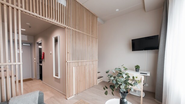 A modern living room with a sofa, a coffee table, a TV mounted on the wall, and a wooden partition.