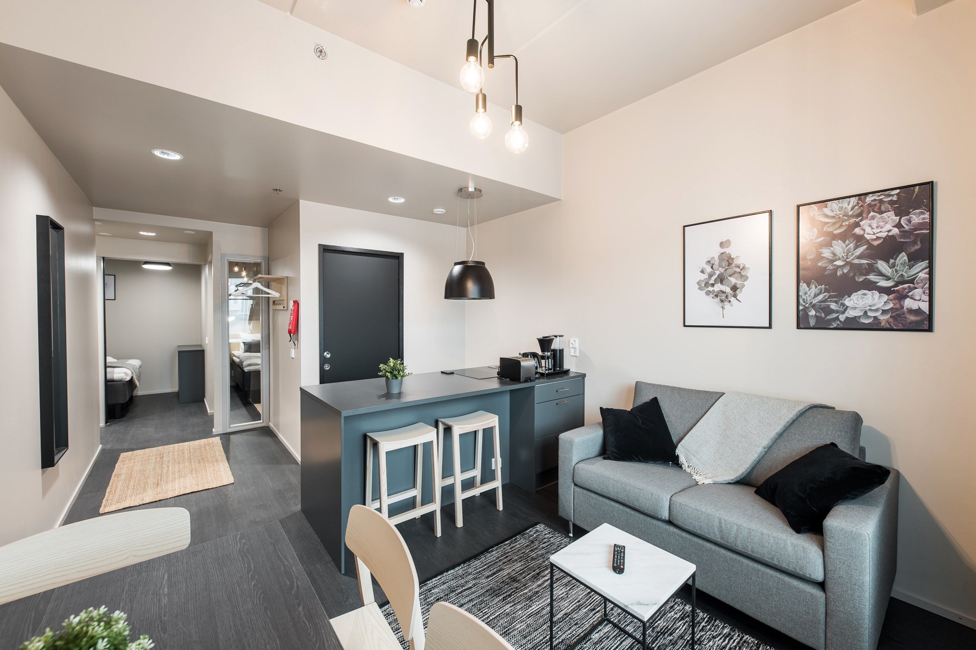 Una sala moderna con un sofá gris, una mesa de centro y una cocina con un taburete de bar.