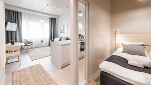 A modern hotel room with a bed, bedside table, and a view of the kitchen area.