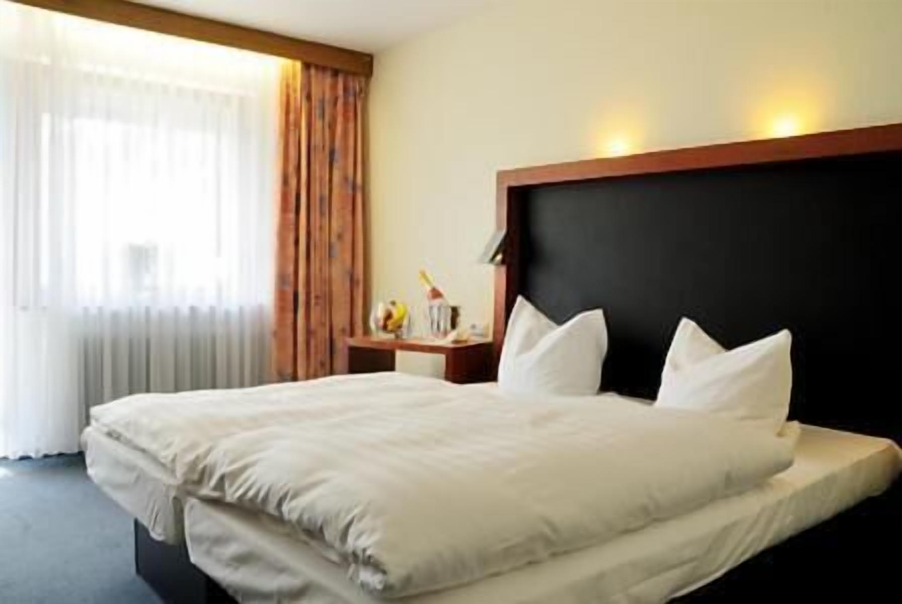 A hotel room with a large bed, a nightstand, and a window with curtains.