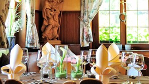 Un coin repas avec une table dressée pour deux personnes, une statue et une grande fenêtre avec des rideaux.