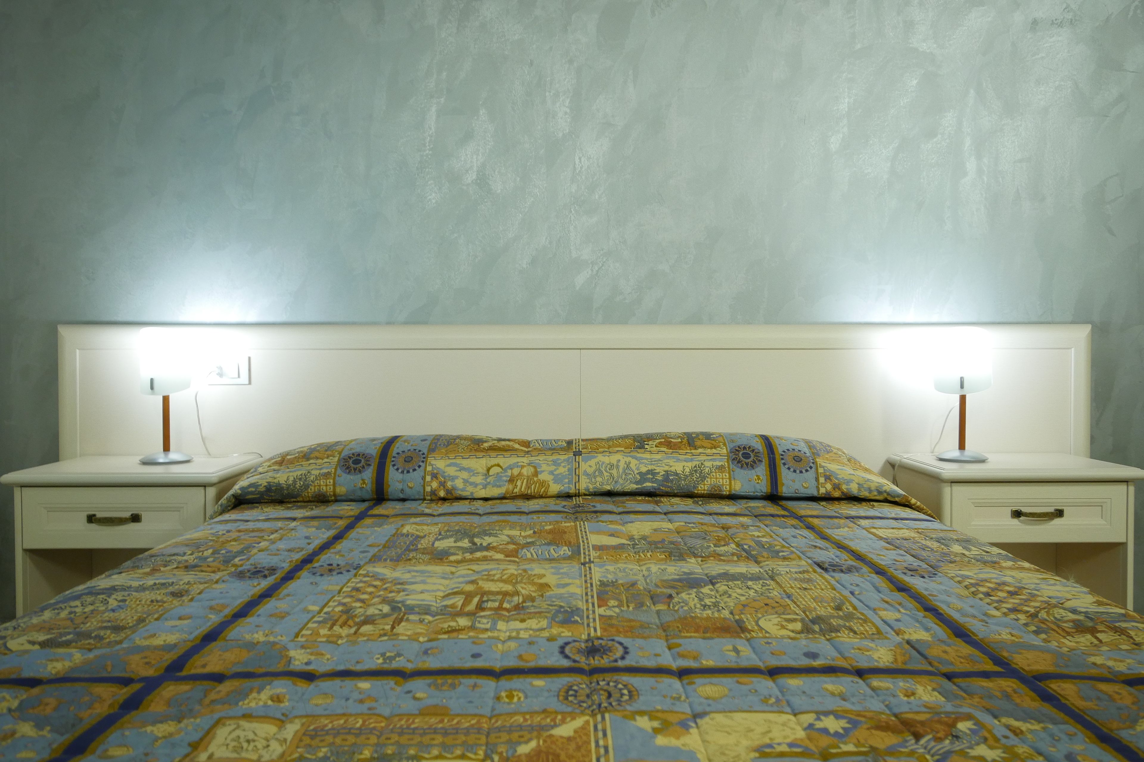 A bed with a patterned bedspread, two bedside tables with lamps, and a textured wall.