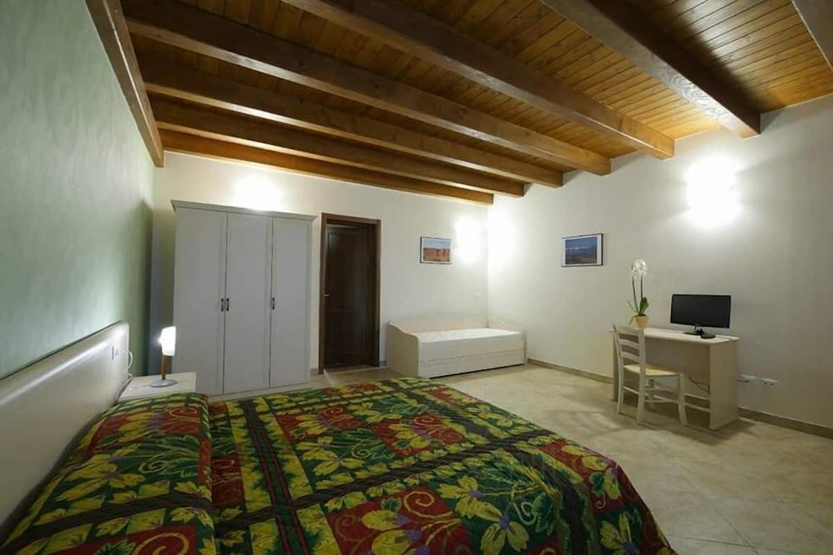 A bedroom with a bed, a desk, a chair, a wardrobe, and a small plant.